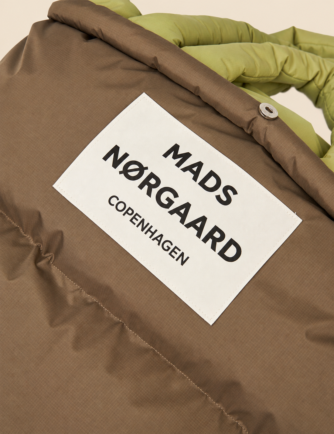 Close-up of the Mads Nørgaard Copenhagen logo patch and padded ripstop fabric on the Green Olive/Tarmac Pillow Bag.