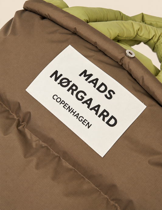 Close-up of the Mads Nørgaard Copenhagen logo patch and padded ripstop fabric on the Green Olive/Tarmac Pillow Bag.