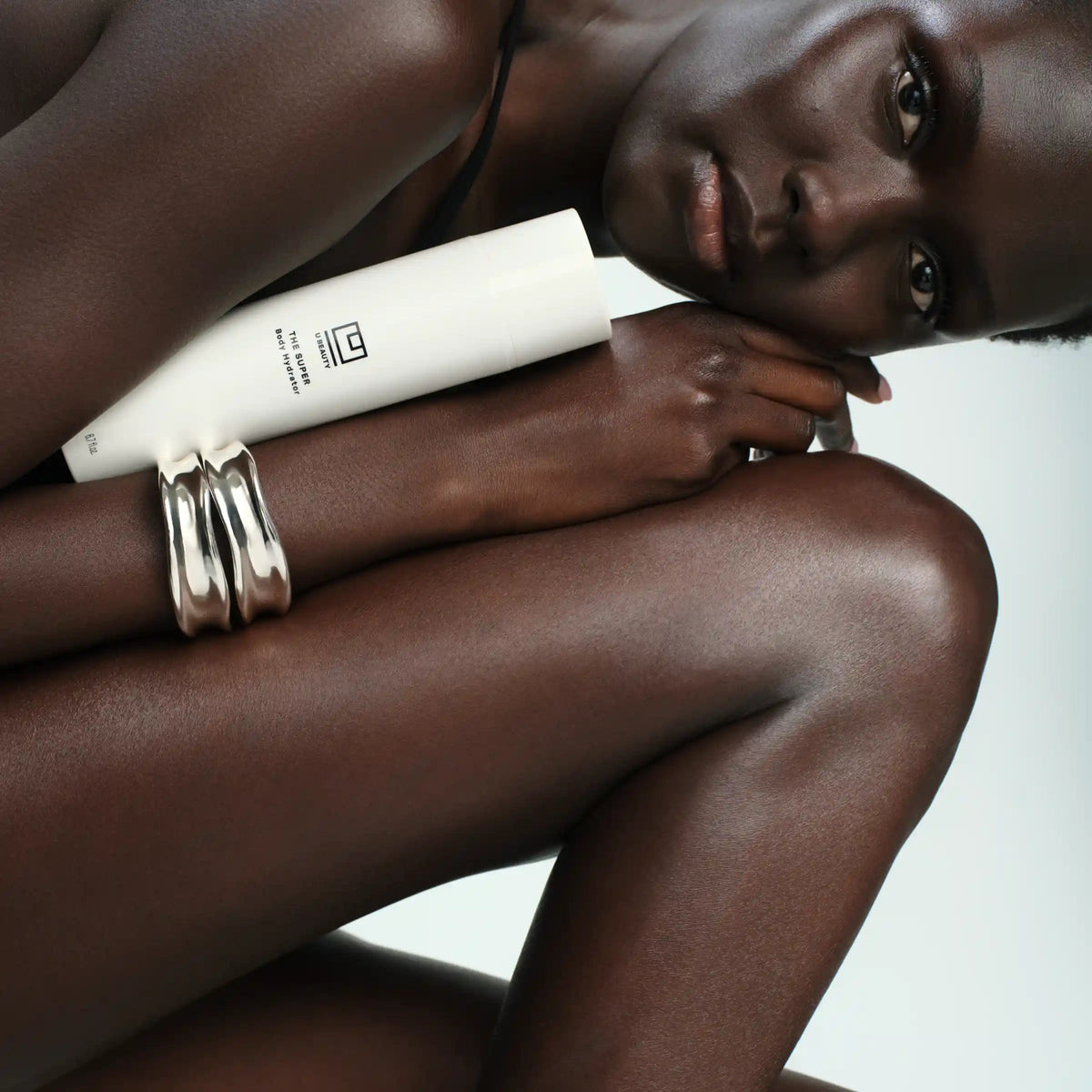 Person holding a skincare product with a brand logo, wearing silver rings on a neutral background